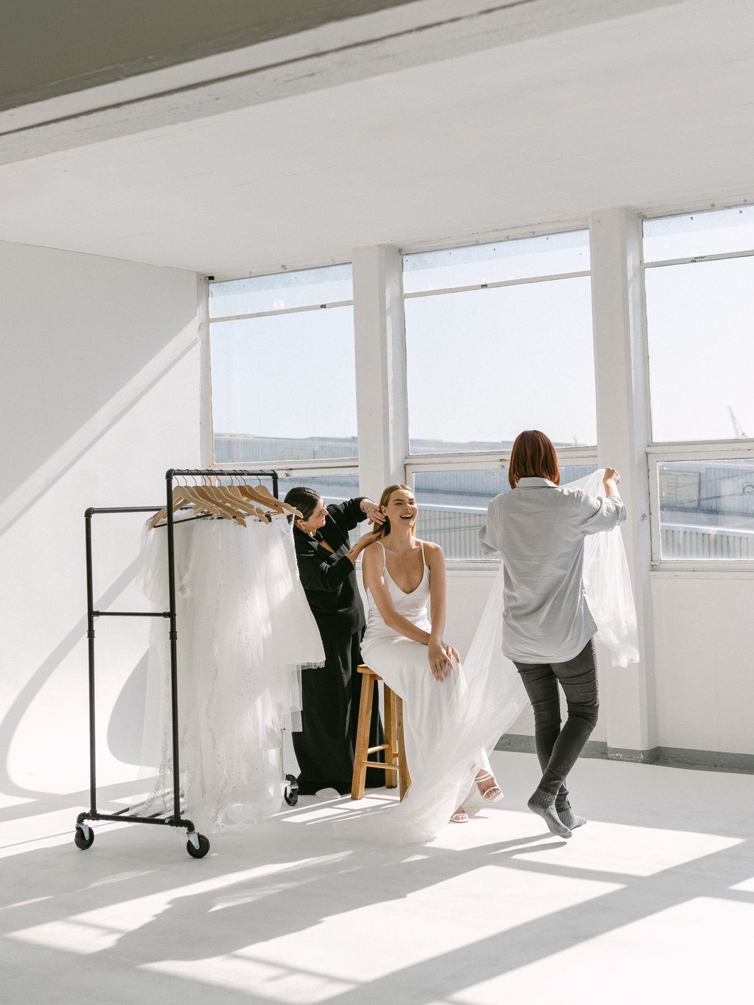 Hair and makeup artist fixing a smiling models hair with a stylist carrying a veil 